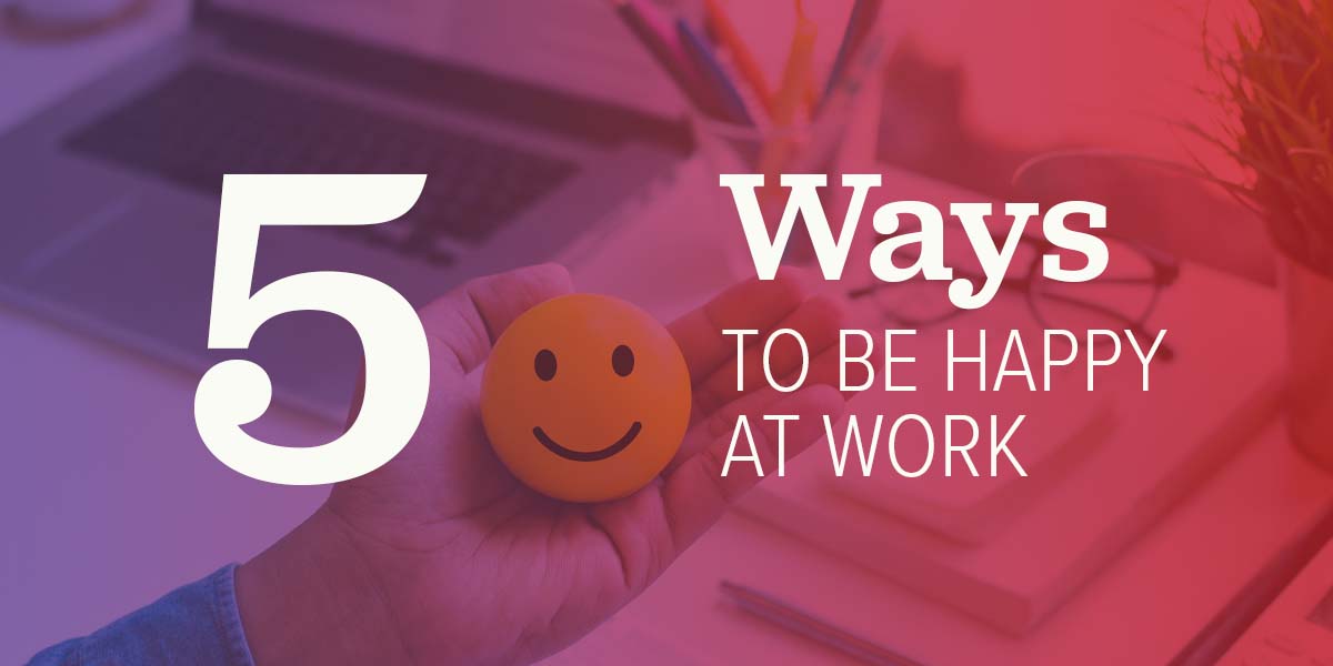 A person holding a smiley face at their work desk.